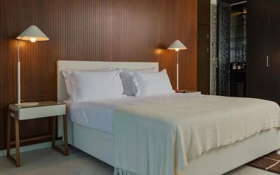 King bedroom featuring white bedding, a wood-panelled feature wall, bedside tables, matching lamps, and dark built-in wardrobes at Prima Millennium.
