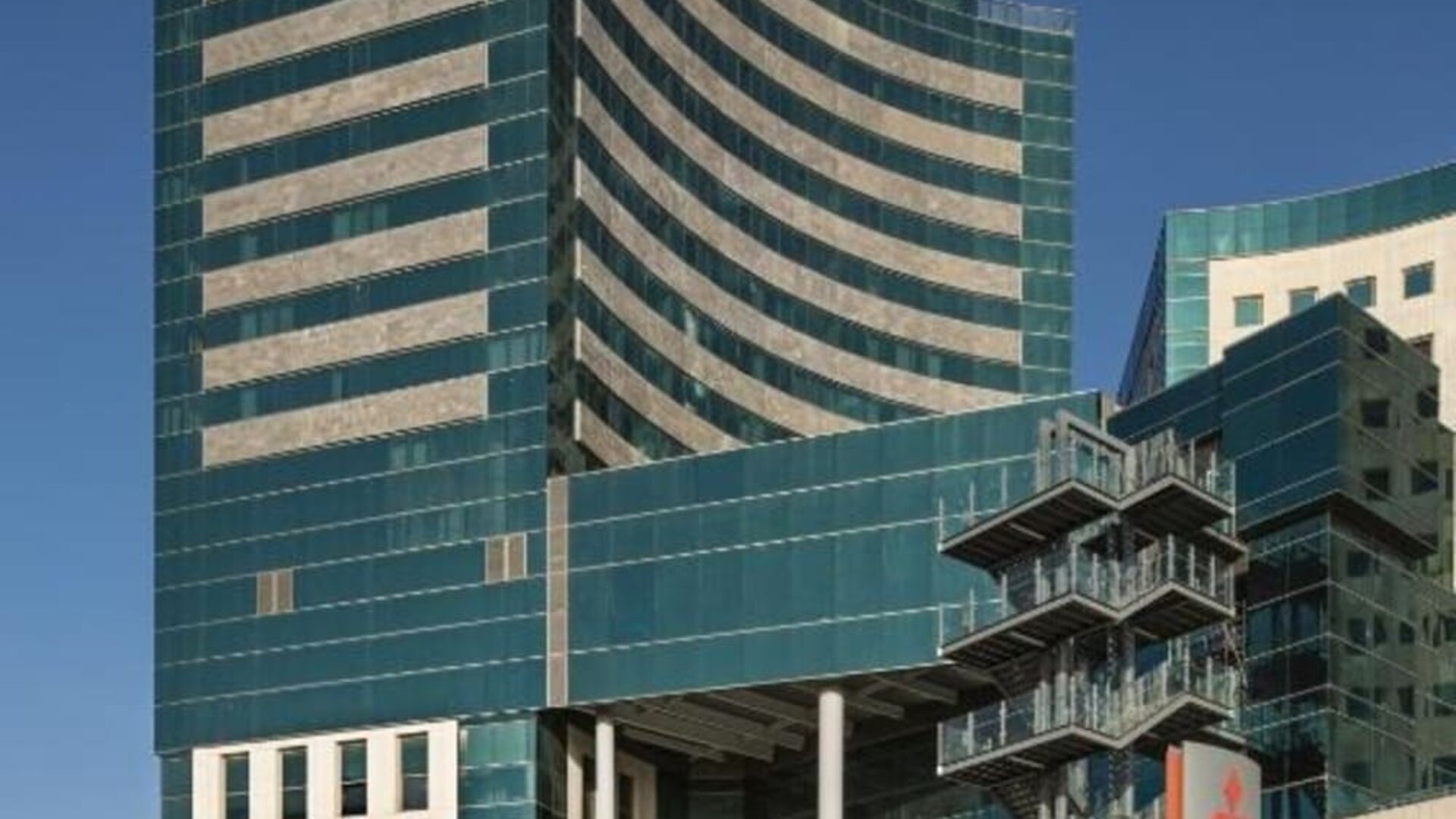 Exterior view of Prima Millennium, a modern multi-storey building with curved green-tinted glass façades, beige horizontal accents, and commercial spaces at street level.