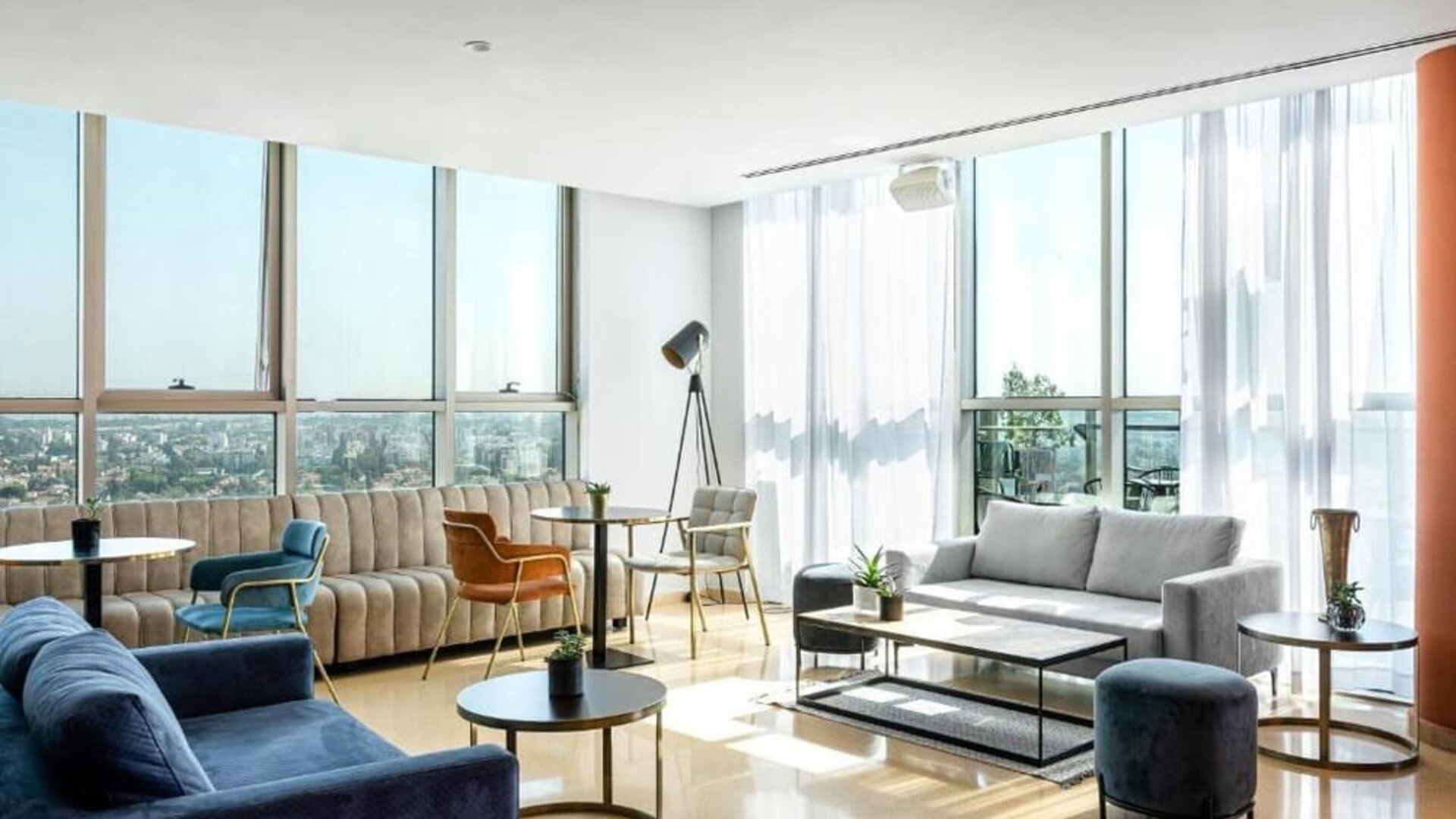 Spacious hotel suite lounge with floor-to-ceiling windows, city views, blue and neutral sofas, accent chairs, and contemporary coffee tables at Prima Millennium.