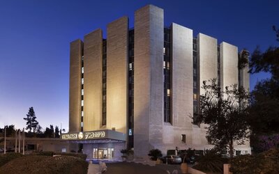Exterior view of Prima Park Hotel at dusk, showing the multi-storey building illuminated against the evening sky, landscaped grounds, and main entrance.