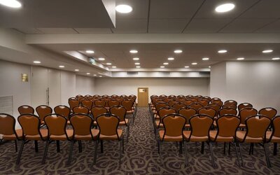 Meeting room arranged classroom-style with rows of chairs, patterned carpeting, a presentation area, and overhead lighting at Prima Park Hotel.