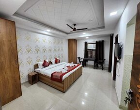 Guest room with a double bed, white bedding, brown and gold accent cushions, a matching bed runner, wooden wardrobe, patterned floral feature wall, and a small seating area by the window at Hotel Urban Abode.