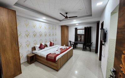 Guest room with a double bed, white bedding, brown and gold accent cushions, a matching bed runner, wooden wardrobe, patterned floral feature wall, and a small seating area by the window at Hotel Urban Abode.