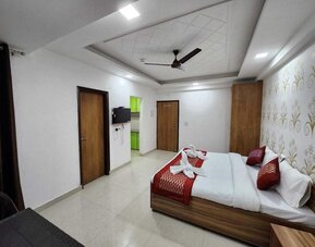 Spacious guest room with a double bed dressed in white bedding and red accent cushions, a red bed runner, decorative feature wall, wooden wardrobes, wall-mounted television, and tiled flooring at Hotel Urban Abode.