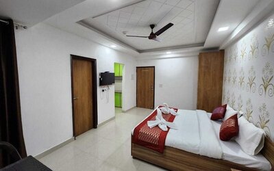 Spacious guest room with a double bed dressed in white bedding and red accent cushions, a red bed runner, decorative feature wall, wooden wardrobes, wall-mounted television, and tiled flooring at Hotel Urban Abode.