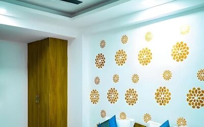 Guest room with a double bed, white bedding, teal and blue accent cushions, a matching bed runner, gold floral wall decorations, wooden wardrobe, and ceiling fan at Hotel Urban Abode.