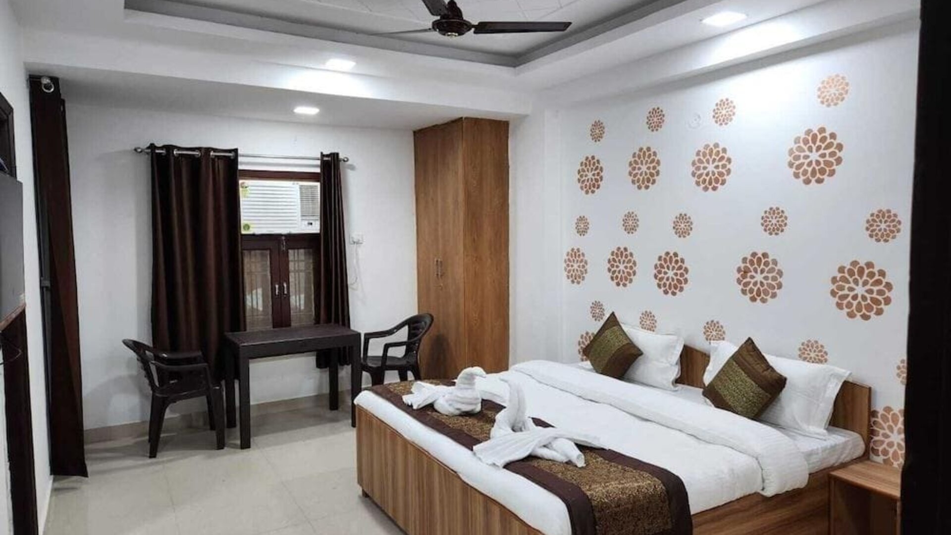Guest room featuring a double bed with white bedding, red and gold accents, decorative towel arrangements, wooden furniture, a wardrobe, and a small table with two chairs at Hotel Urban Abode.