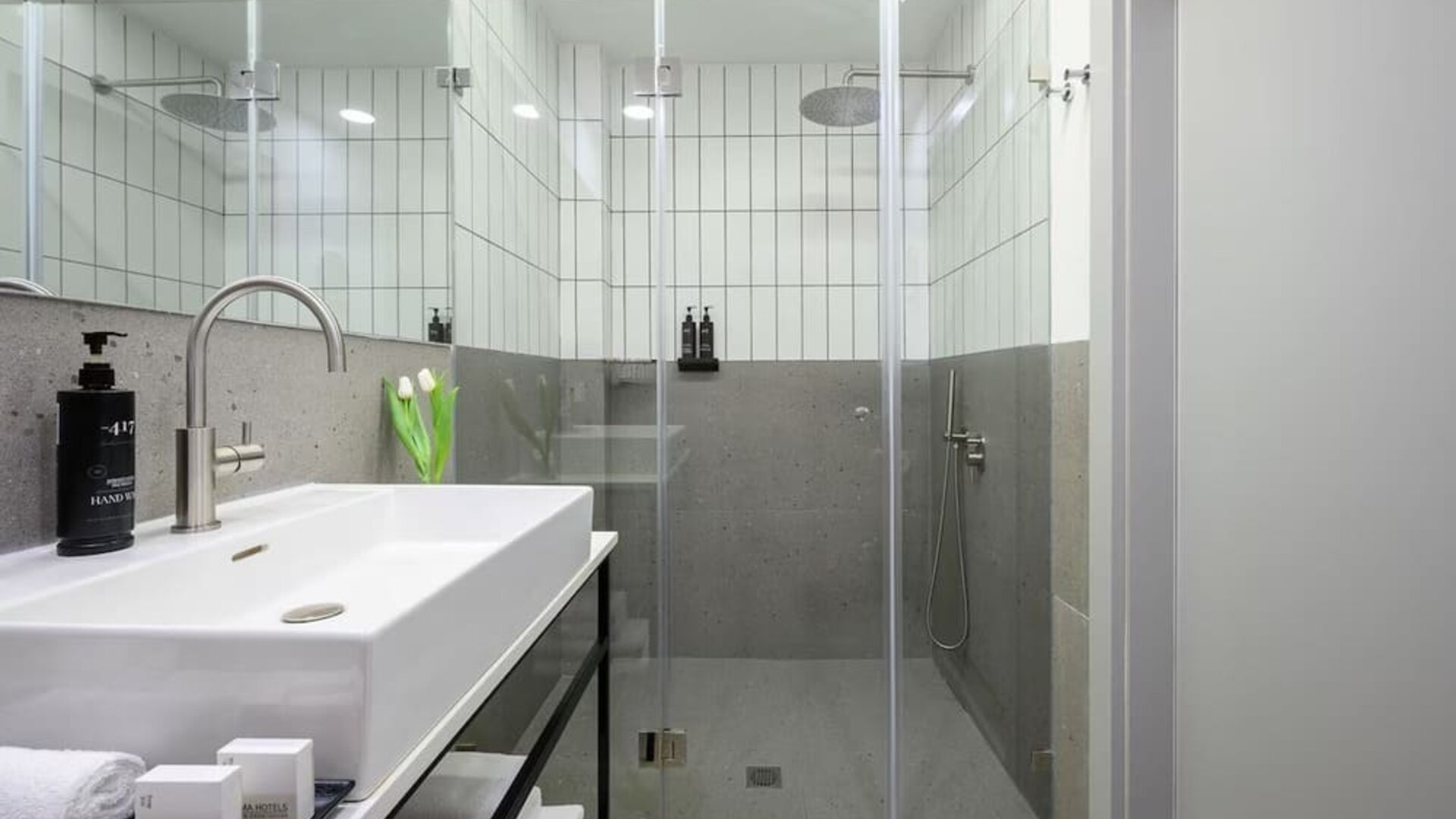 Walk-in shower with glass doors, rainfall showerhead, tiled walls and white vanity at Prima Link.