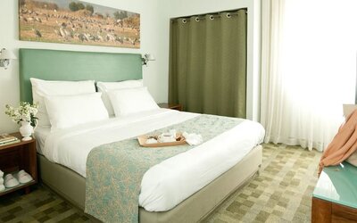 Guest bedroom featuring a king bed, sage-green headboard, patterned runner and bright windows at Prima Galil Tiberias.