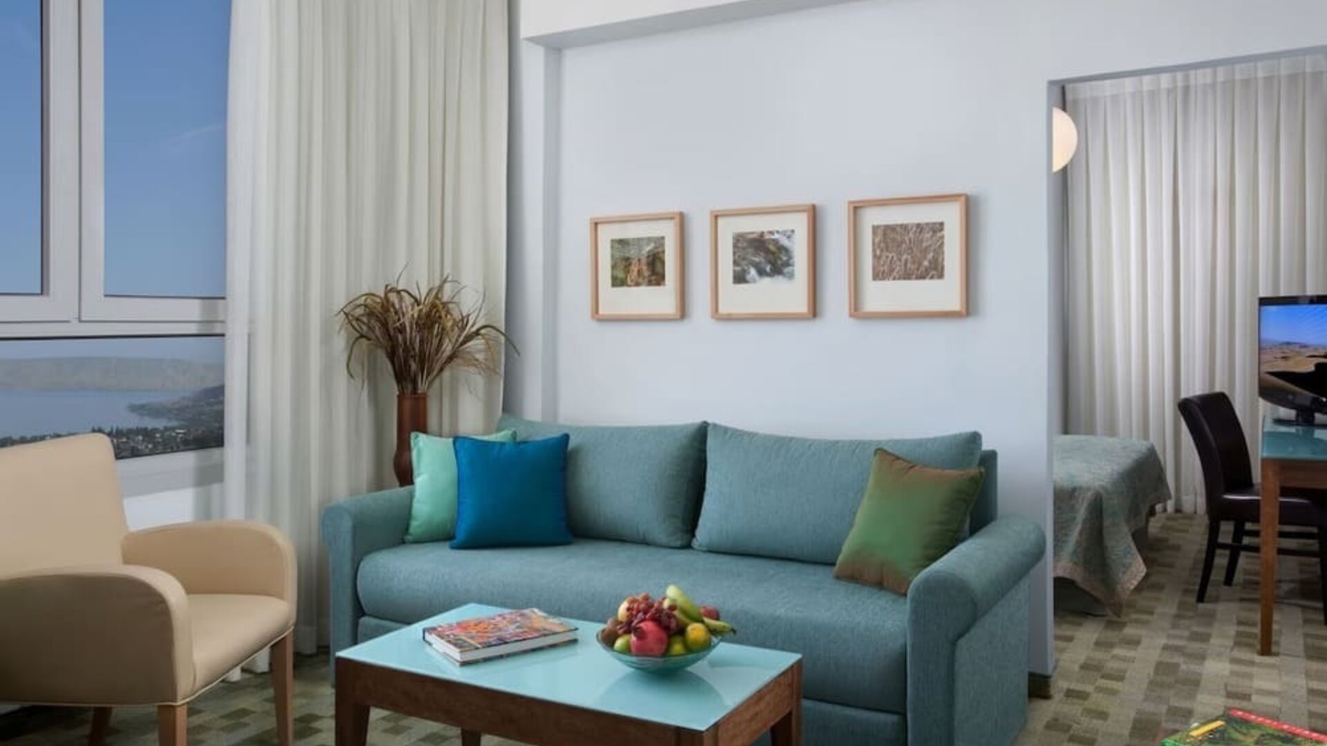 Suite living area with a turquoise sofa, colourful cushions and scenic views through large windows at Prima Galil Tiberias.