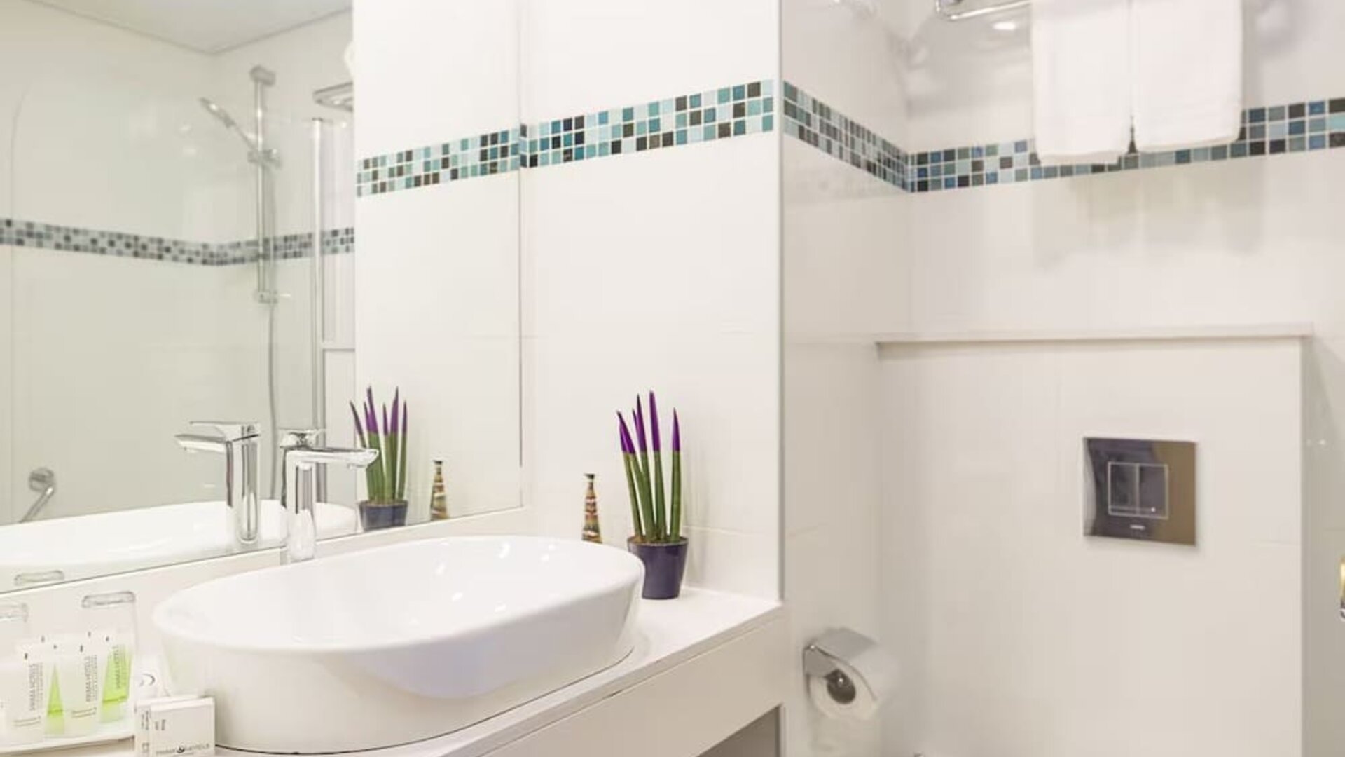 Bathroom with a white vessel sink, large mirror, chrome fixtures and blue-and-green mosaic tile accents at Prima Music Eilat.