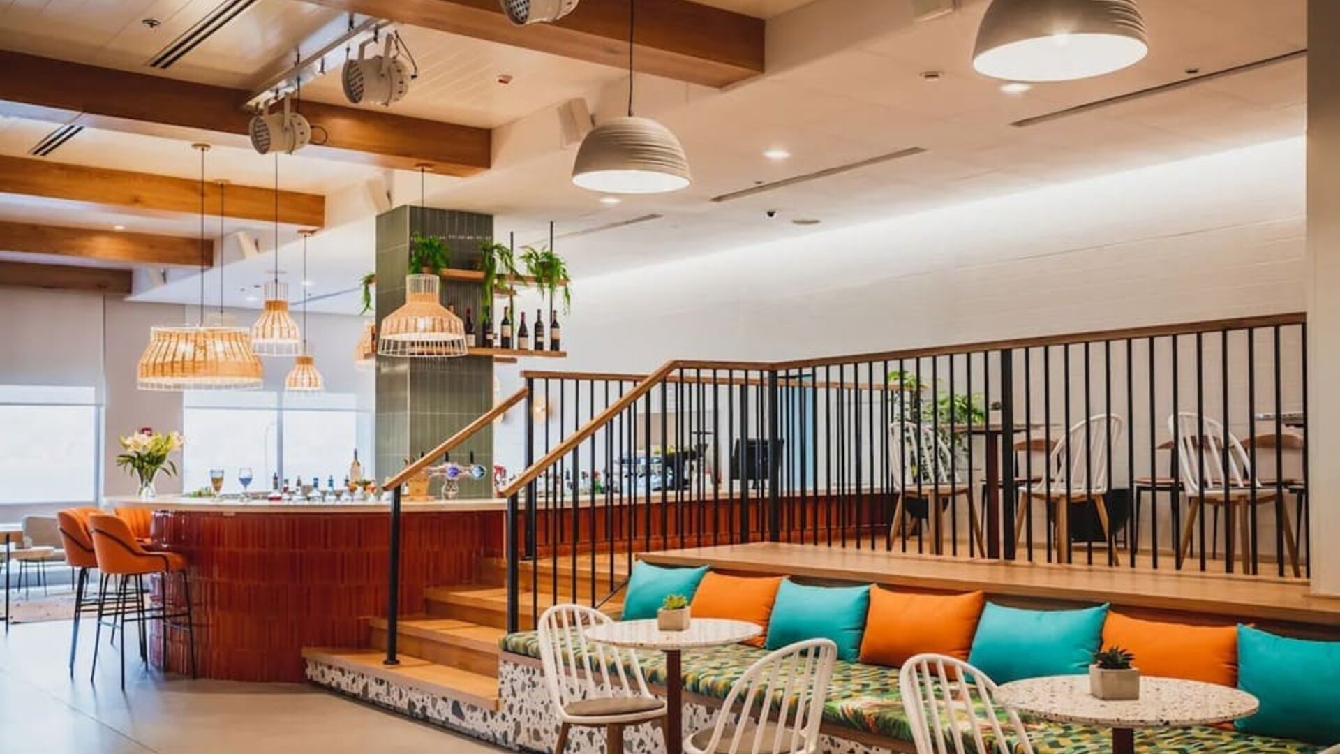 Restaurant lounge with a raised seating area, orange and turquoise cushions, woven chairs and pendant lighting at Prima Music Eilat.