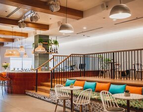 Restaurant lounge with a raised seating area, orange and turquoise cushions, woven chairs and pendant lighting at Prima Music Eilat.