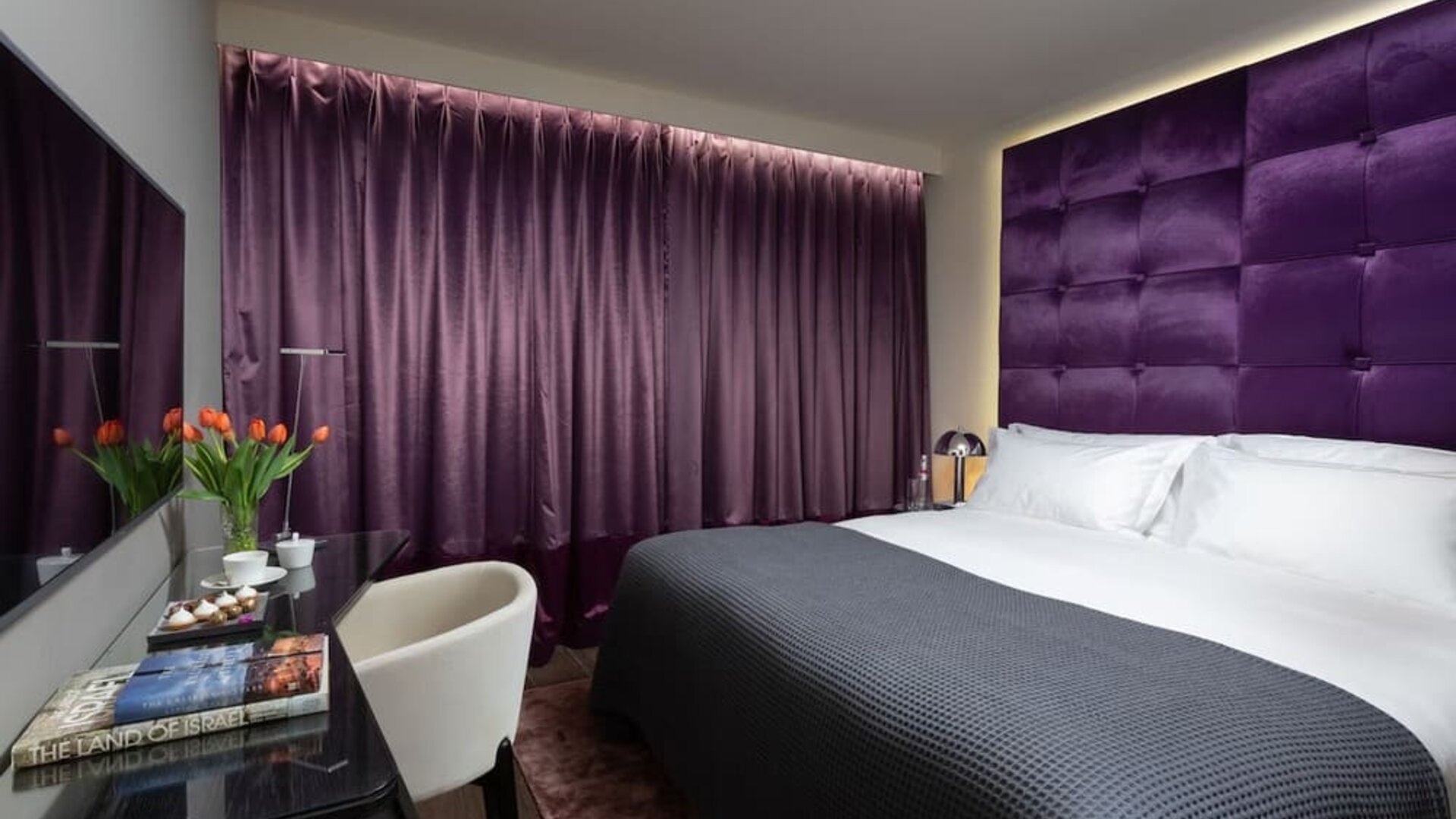 Guest room with king bed, purple upholstered headboard, matching curtains and work desk at Lady Stern Hotel.