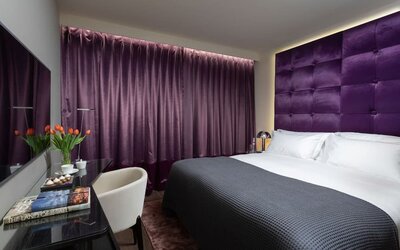 Guest room with king bed, purple upholstered headboard, matching curtains and work desk at Lady Stern Hotel.