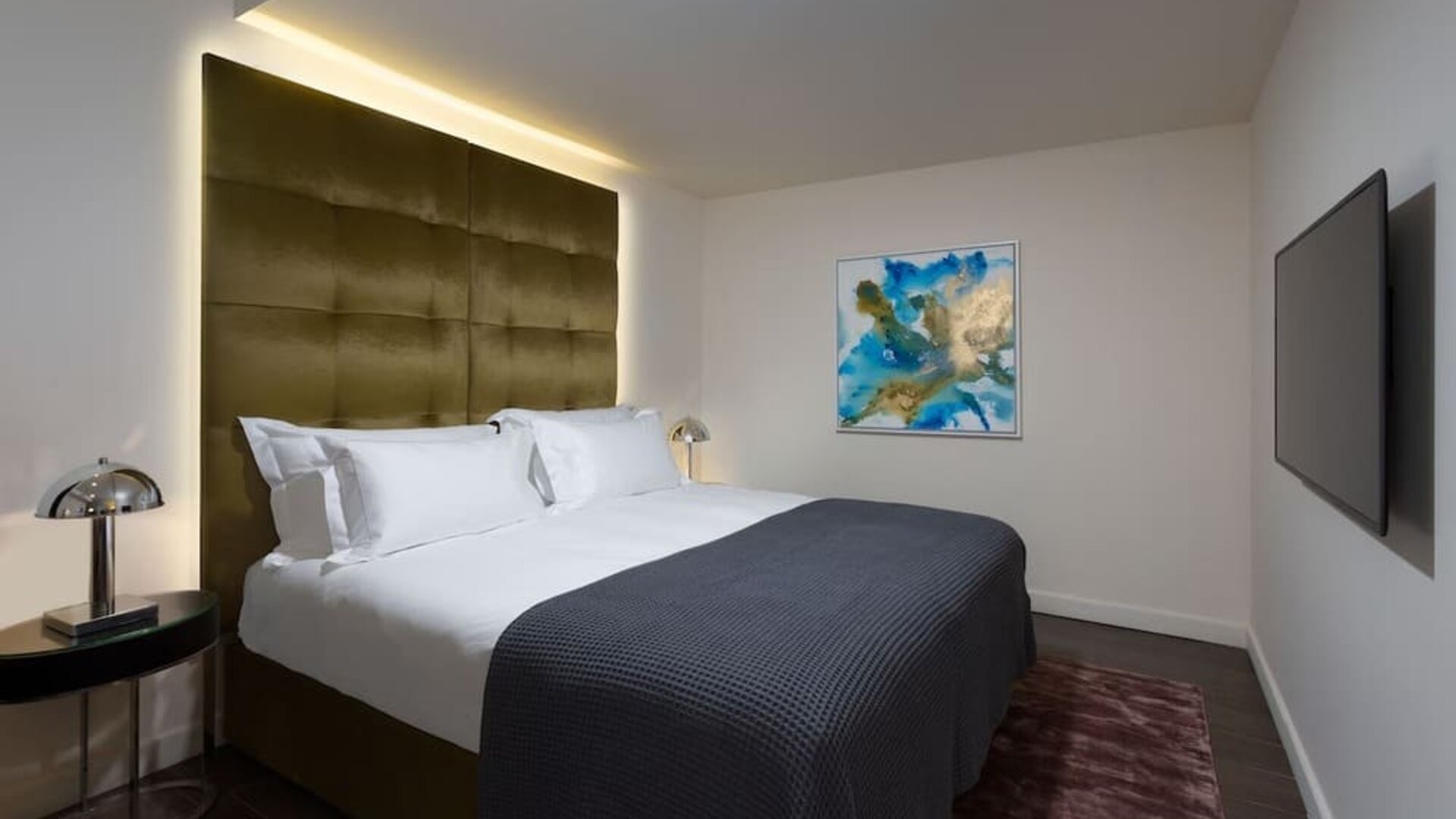 Guest room with king bed, gold upholstered headboard, bedside tables and wall-mounted television at Lady Stern Hotel.