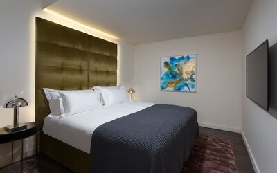 Guest room with king bed, gold upholstered headboard, bedside tables and wall-mounted television at Lady Stern Hotel.