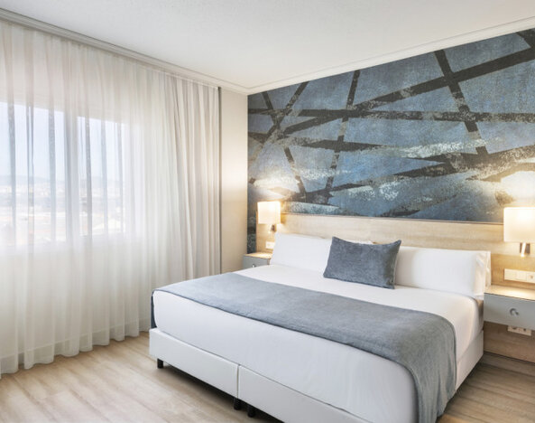 King-size bed with white bedding, grey accents, sheer curtains and a dark abstract feature wall at Hotel Sallés Ciutat del Prat.