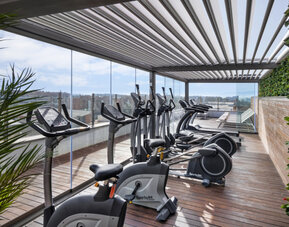 Rooftop fitness centre equipped with stationary bikes, treadmills and exercise machines beside glass railings at Hotel Sallés Ciutat del Prat.