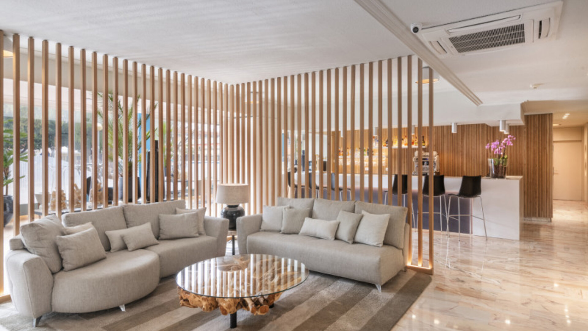 Lounge area featuring curved grey sofas, a round wooden coffee table and decorative timber screens at Hotel Sallés Ciutat del Prat.