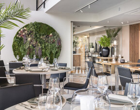 Restaurant dining room with wooden tables, black chairs, place settings and warm illuminated wall panels at Hotel Sallés Ciutat del Prat.