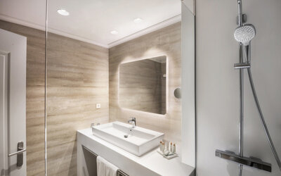 Modern bathroom with a glass shower enclosure, white vanity basin, illuminated mirror and beige tiled walls at Hotel Sallés Ciutat del Prat.