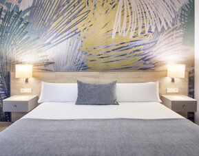 Double bed dressed in white linens and grey accents, flanked by bedside tables and wall lamps at Hotel Sallés Ciutat del Prat.
