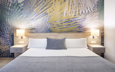 Double bed dressed in white linens and grey accents, flanked by bedside tables and wall lamps at Hotel Sallés Ciutat del Prat.