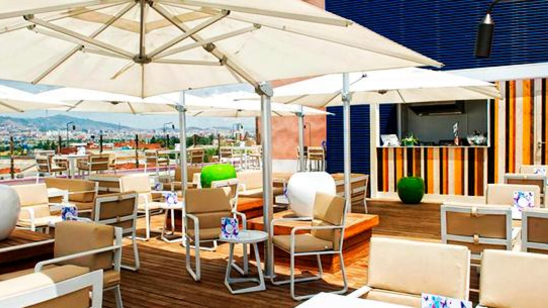 Rooftop terrace with white parasols, wooden tables, outdoor seating and city views at Hotel Sallés Ciutat del Prat.