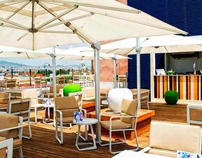 Rooftop terrace with white parasols, wooden tables, outdoor seating and city views at Hotel Sallés Ciutat del Prat.