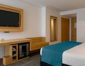 Guest room with white bedding, teal bed runner, wall-mounted television and work desk at Sonesta Hotel Bogotá.