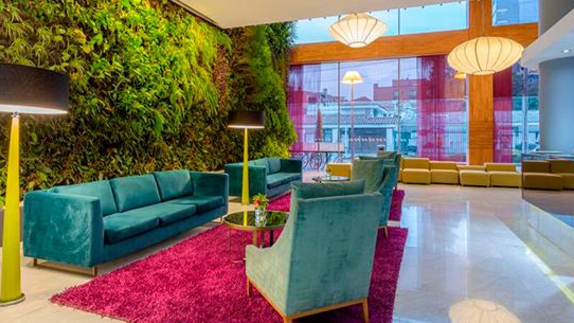 Contemporary lounge with teal sofas, colourful armchairs, magenta rug and vertical garden at Sonesta Hotel Bogotá.