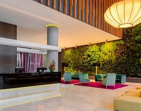 Reception area with dark front desk, green living wall, orange seating and decorative pendant lights at Sonesta Hotel Bogotá.