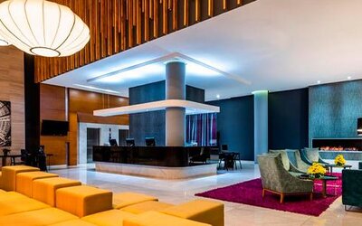 Hotel lobby with reception desk, orange lounge seating, wood accents and contemporary pendant lights at Sonesta Hotel Bogotá.