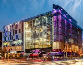 Modern glass-fronted hotel exterior illuminated with purple lighting against the evening sky at Sonesta Hotel Bogotá.