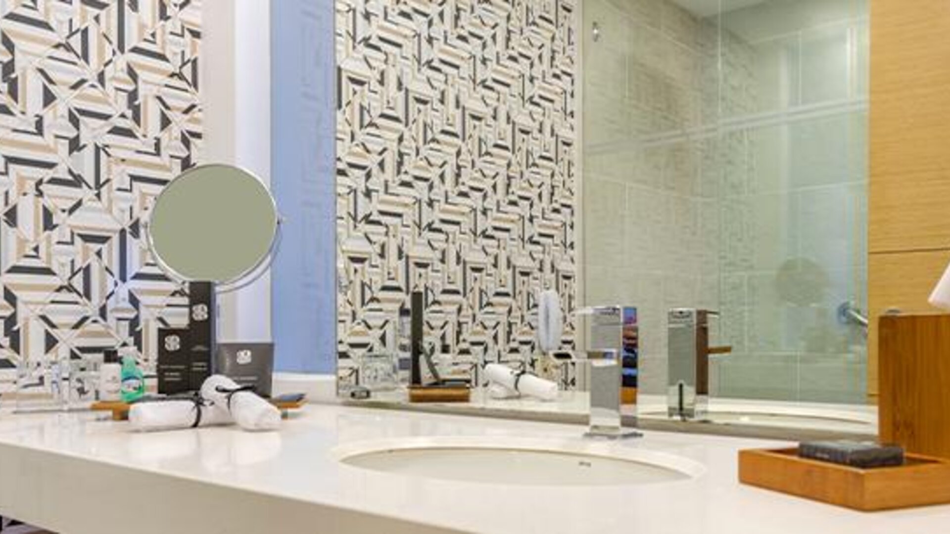 Bathroom vanity with white countertop, round vessel sink, mirror and geometric-patterned wall tiles at Sonesta Hotel Bogotá.
