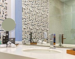 Bathroom vanity with white countertop, round vessel sink, mirror and geometric-patterned wall tiles at Sonesta Hotel Bogotá.