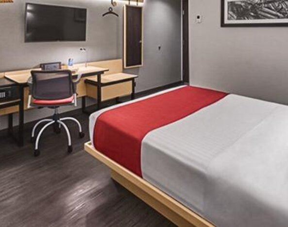Guest room with a double bed, red runner, wall-mounted television, wooden desk and shelving at City Express by Marriott CDMX La Villa.