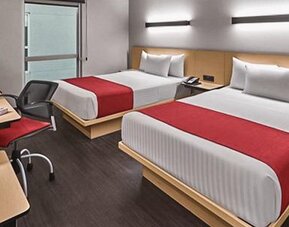 Guest room with two beds, red bed runners, wooden headboards, bedside lighting and a work desk at City Express by Marriott CDMX La Villa.