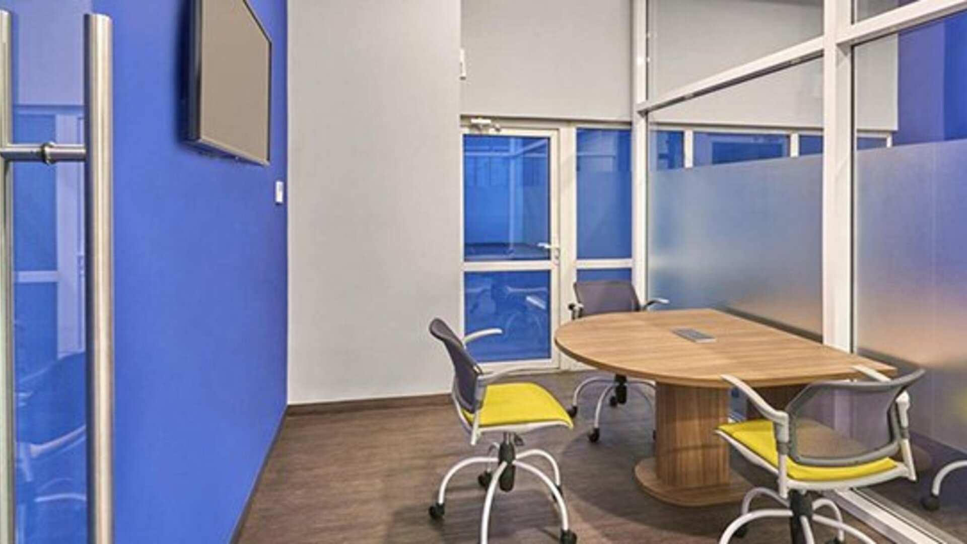 Meeting room with oval conference table, office chairs, wall-mounted television and blue accent wall at City Express by Marriott CDMX La Villa.