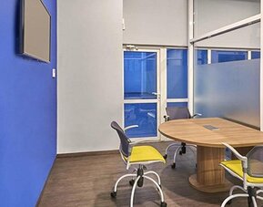 Meeting room with oval conference table, office chairs, wall-mounted television and blue accent wall at City Express by Marriott CDMX La Villa.