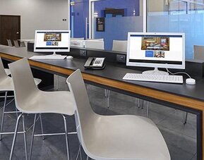 Business centre with desktop computers, white chairs and a long counter beside floor-to-ceiling windows at City Express by Marriott CDMX La Villa.