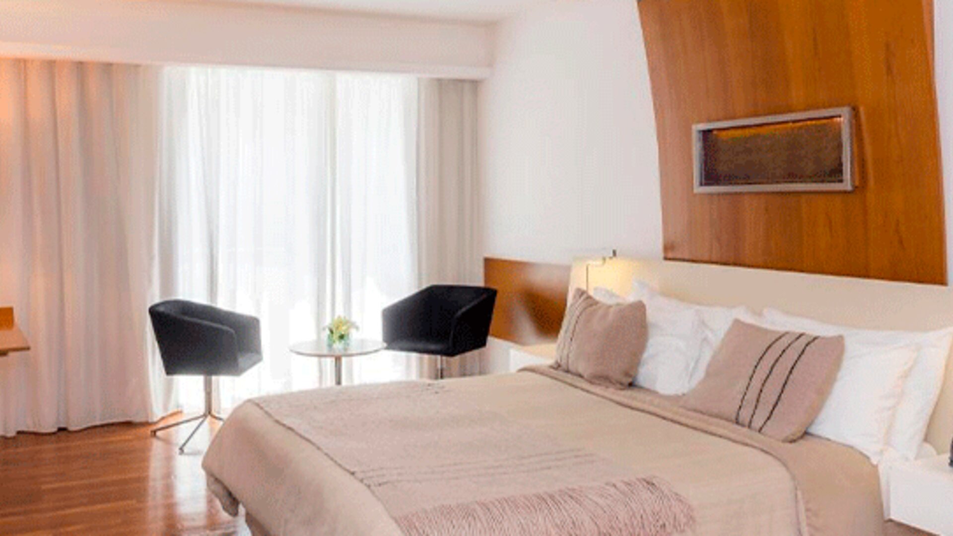 Guest room with king-size bed, neutral bedding, wooden accent wall, bedside tables and seating area at Design Suites Buenos Aires.