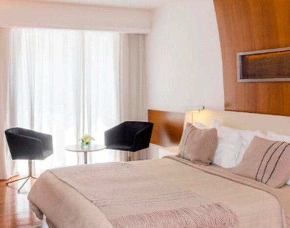 Guest room with king-size bed, neutral bedding, wooden accent wall, bedside tables and seating area at Design Suites Buenos Aires.