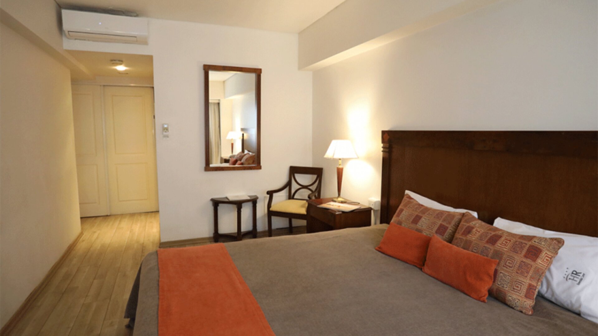Guest room with king bed, patterned cushions, orange bed runner, wooden headboard and bedside lamps at HR Esmeralda Luxor.