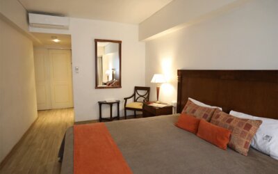 Guest room with king bed, patterned cushions, orange bed runner, wooden headboard and bedside lamps at HR Esmeralda Luxor.