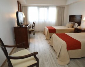 Twin guest room with two beds, orange runners, wooden furniture, television and large curtained windows at HR Esmeralda Luxor.