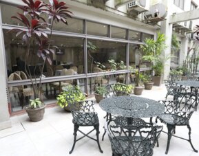 Outdoor terrace with decorative black metal tables and chairs beside large windows and potted plants at HR Esmeralda Luxor.