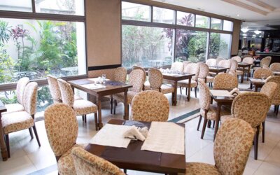 Dining room with patterned upholstered chairs, wooden tables, white tiled floors and large garden-facing windows at HR Esmeralda Luxor.