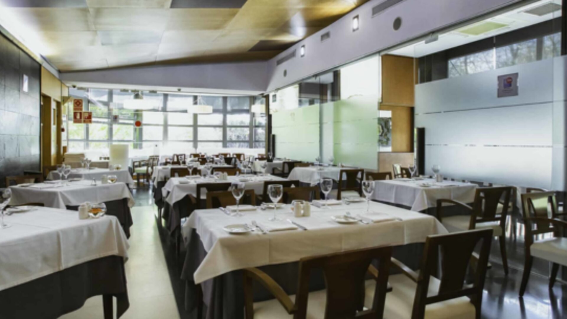 Restaurant dining room with white tablecloths, dark wooden chairs, glass walls and neatly arranged place settings at Hotel Best Western PLUS Alfa Aeropuerto.
